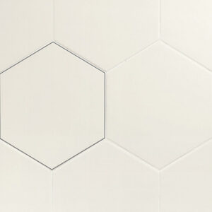 Modern bathroom with white hexagonal tile walls, a sleek chrome wall-mounted faucet, and a white sink beneath a window. A lit candle is visible in the corner.