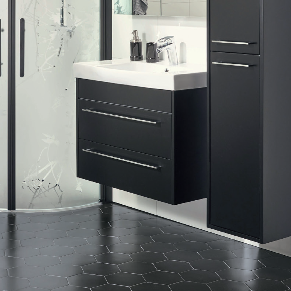 Modern bathroom with black hexagon tile floor, floating vanity with two drawers, white sink, black toiletries, tall black cabinet, and glass shower with frosted plant designs.