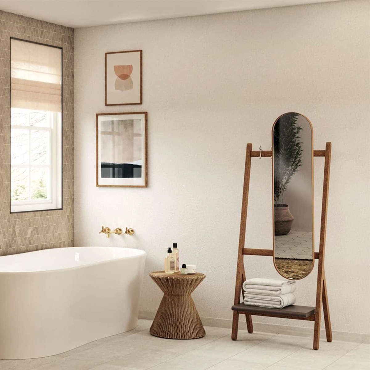 A modern bathroom featuring the Boho - Bone freestanding tub, complemented by wall art, a small round side table with toiletries, and a wooden standing mirror with shelves displaying rolled towels. The neutral, minimalist decor is enhanced by natural light.