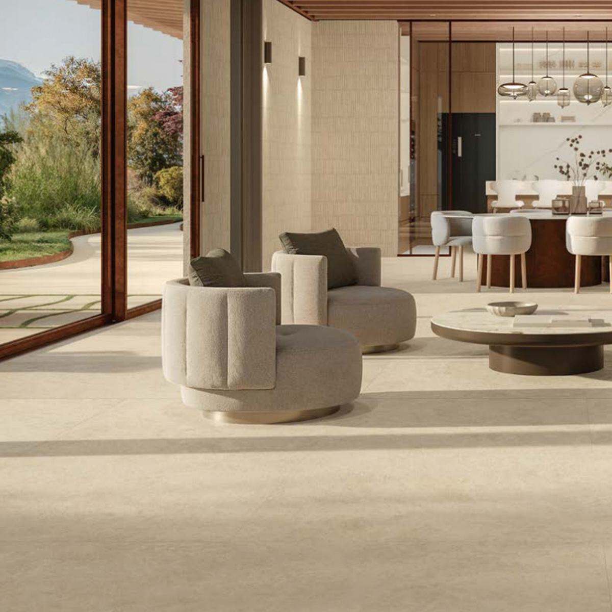 A modern living room features large windows, round gray chairs, a low coffee table, and a dining area in the background. The space is filled with natural light and offers views of greenery outside, all beautifully complemented by Boost Icor - Dune flooring.