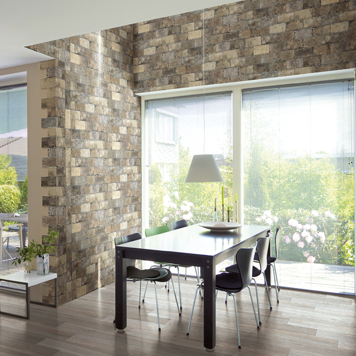 Modern dining room with a stone-look brick tile accent wall and column in mixed brown and beige tones, paired with a white dining table, dark chairs, a pendant light, and floor-to-ceiling windows overlooking a garden.