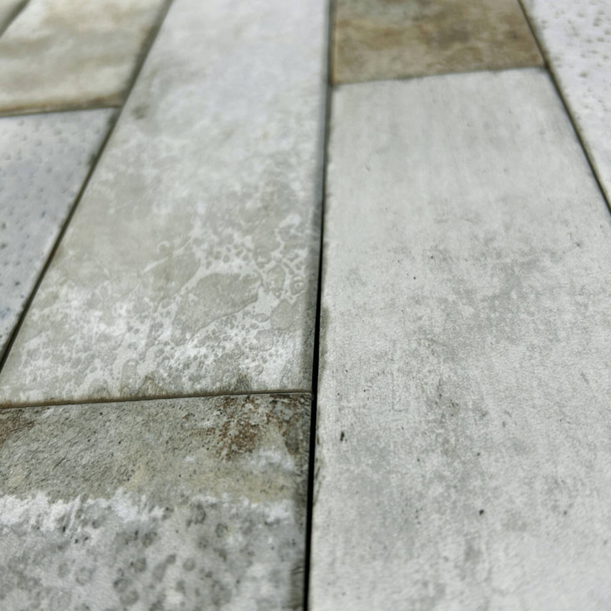Close-up of Pals rectangular concrete tiles arranged in a staggered pattern. The tiles display varying shades of gray and subtle textures, with some brown stains or discoloration visible due to weathering.