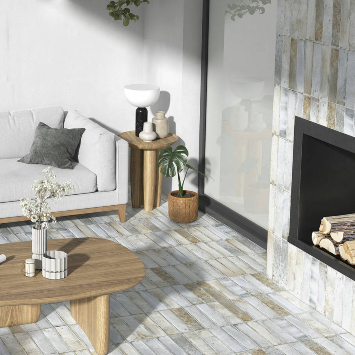 A modern living room featuring the Pals light gray sofa, a wooden coffee table, matching side table, potted plant, decorative objects, and a fireplace stacked with logs. Sunlight streams in through a large window.