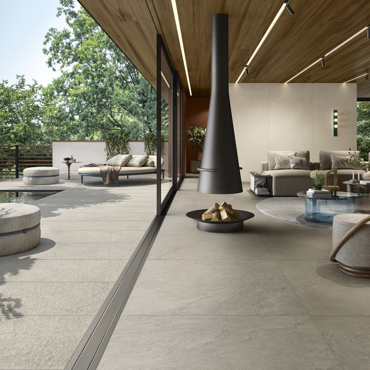 A modern indoor-outdoor living space featuring Pulse - Clay, highlighted by a sleek fireplace, comfortable seating, a wooden ceiling, large glass doors, and a patio with lounge chairs surrounded by trees and greenery.