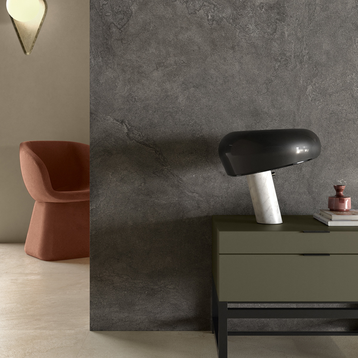 A modern interior featuring the Pulse - Shadow, a rust-colored chair, a textured grey wall, an olive green side table, a black and white marble lamp, stacked books, and a small decorative object.
