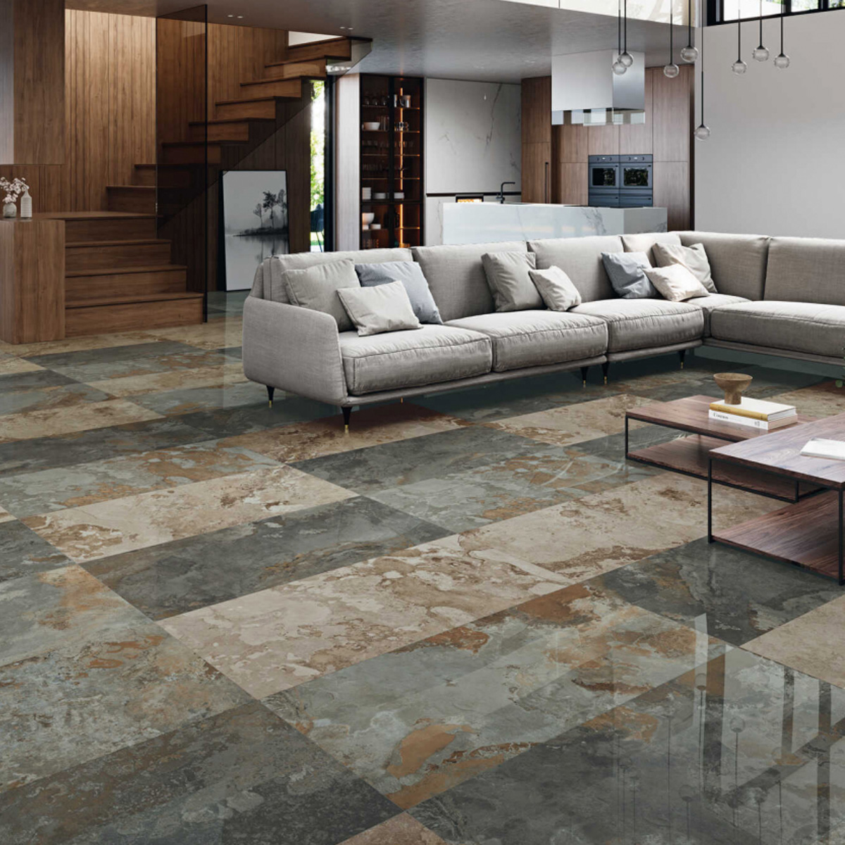 A modern living room with a large gray sectional sofa, a low wooden coffee table, and a checkered Yukatan Polished – Multicolor stone tile floor. Wooden stairs and kitchen cabinets are visible in the background.