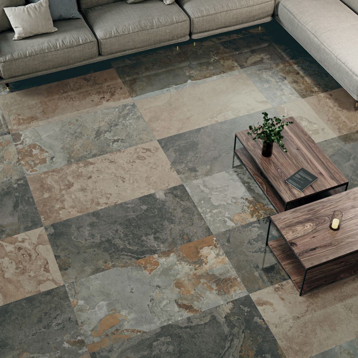 A modern living room with large Yukatan Polished – Multicolor stone-patterned tile flooring, a sectional beige sofa, two stacked wooden coffee tables, a potted plant, and a decorative tray, viewed from above.