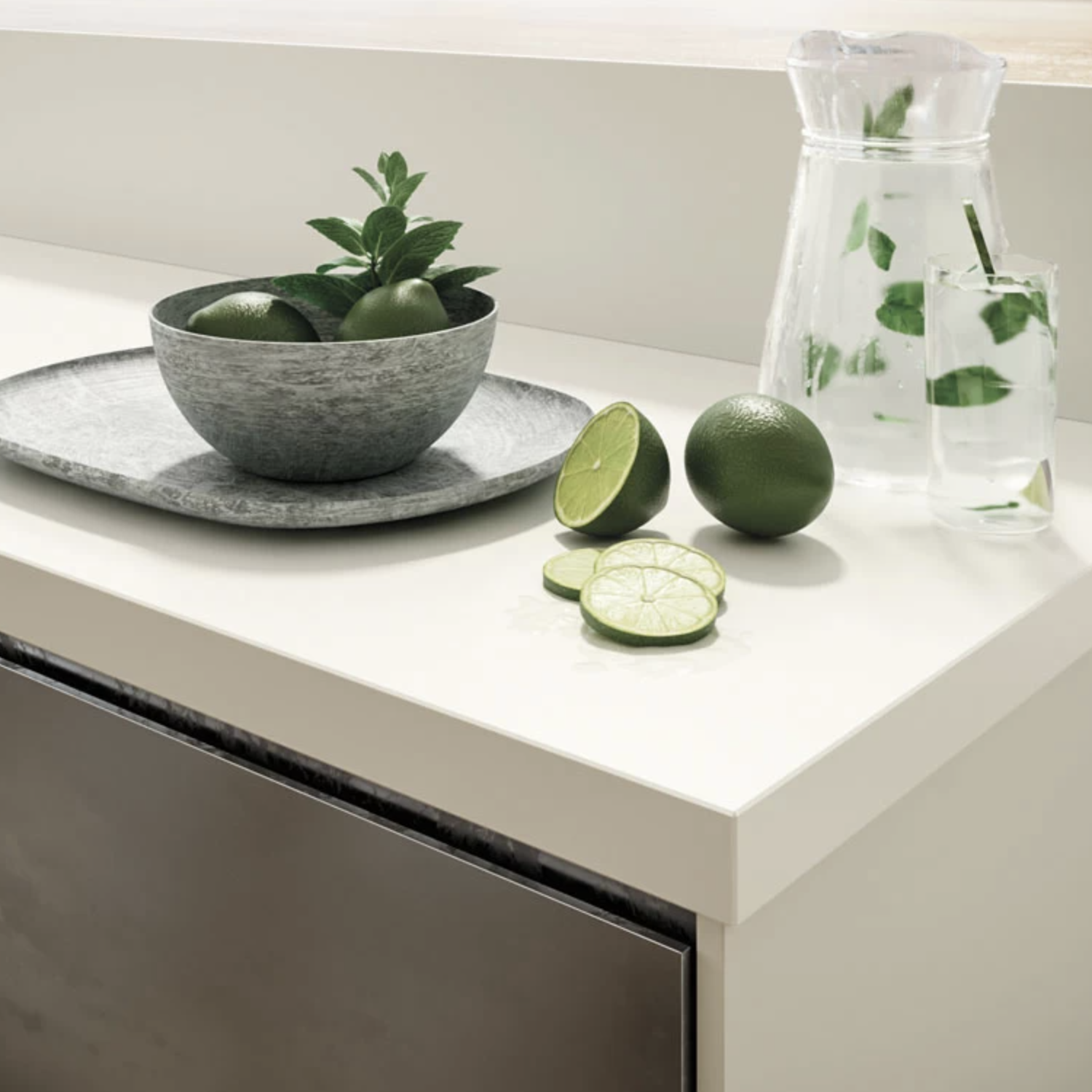 An Absolute White countertop featuring a gray bowl of limes and mint, sliced limes on a tray, a glass pitcher of water with mint, and a glass of water with a straw and mint.