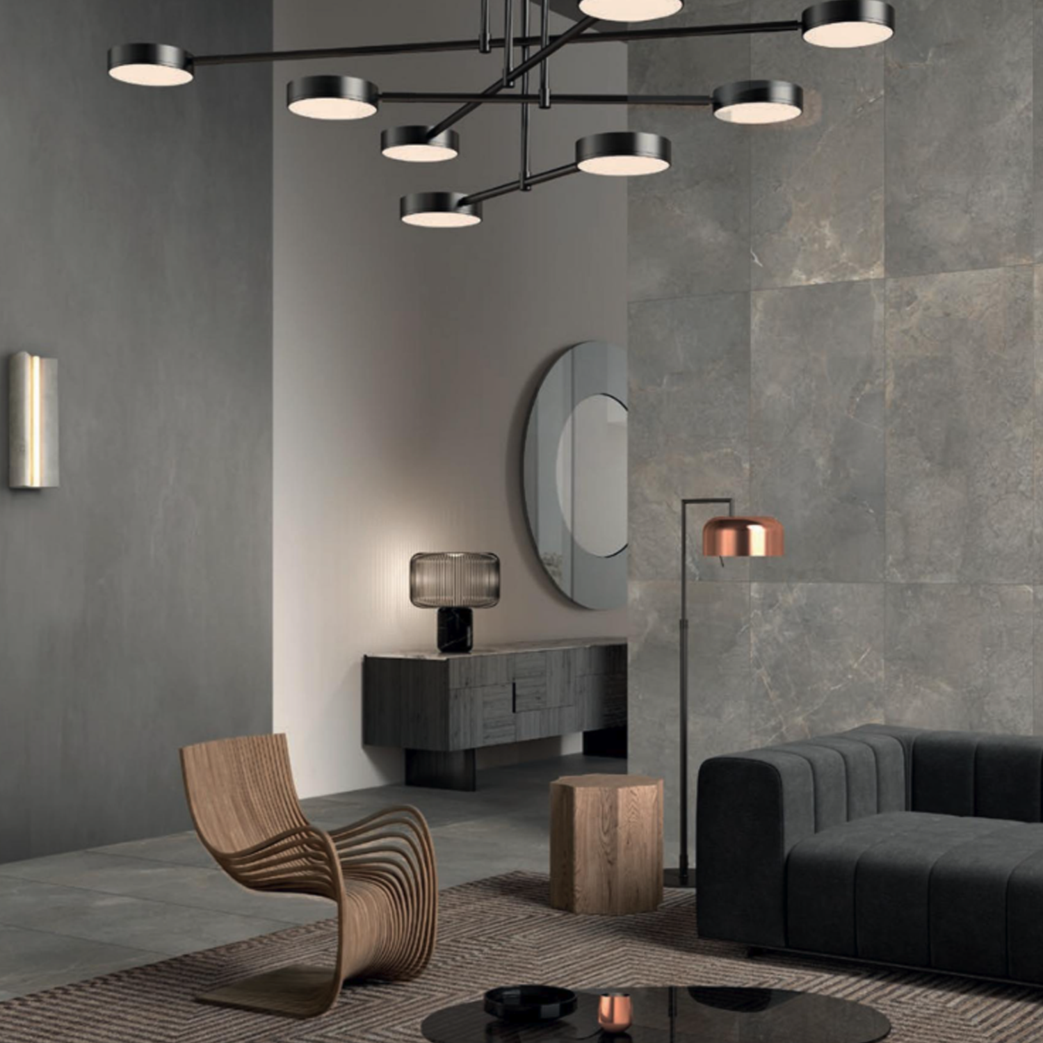 Modern living room featuring Anthology/Anthea - Earth wallpapers on the textured gray walls and floor, complemented by a dark sofa, curved wooden chair, round coffee table, geometric floor lamp, sideboard with lamp, large round mirror, and minimalist chandelier.