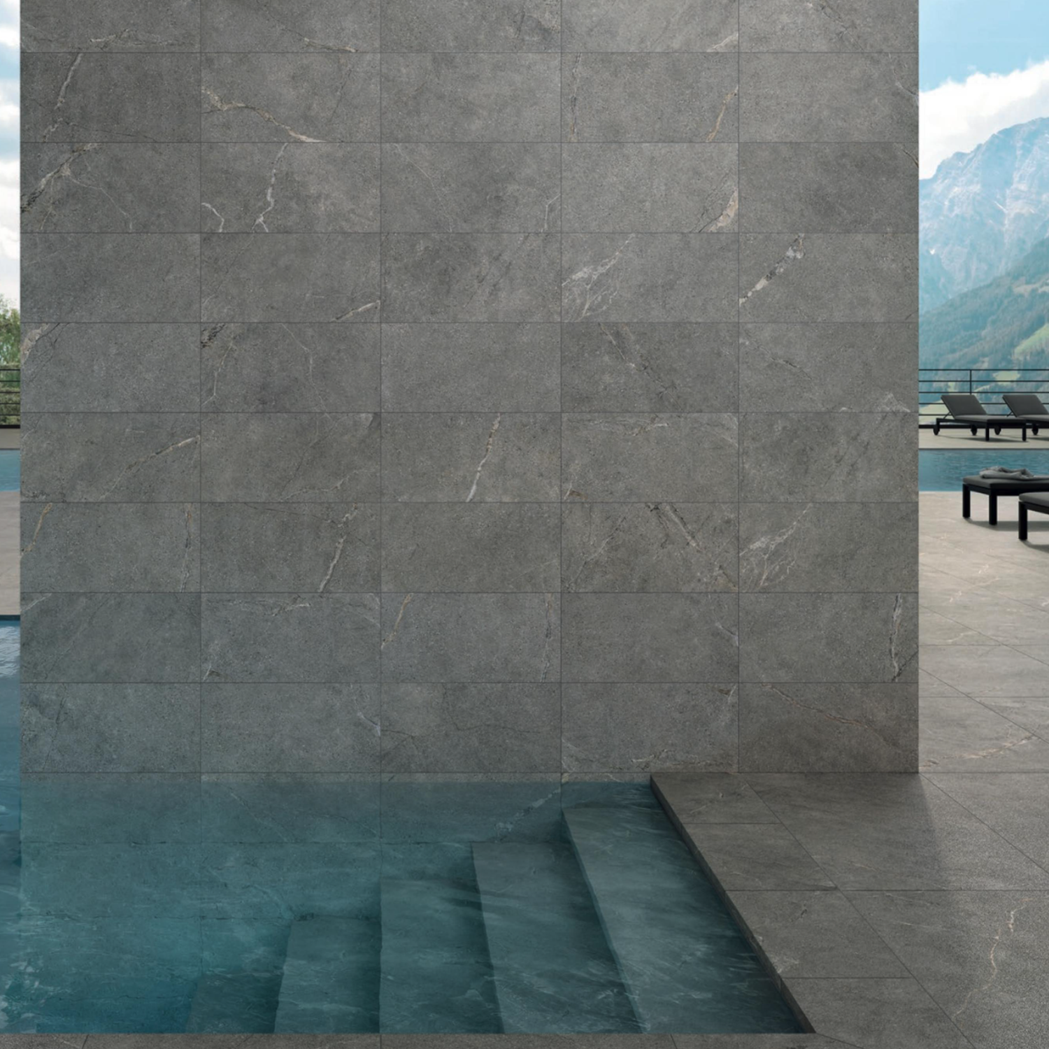 Anthology/Anthea - Gray stone tile wall and submerged steps lead into a clear blue pool; outdoor patio with lounge chairs and a mountain landscape visible in the background.