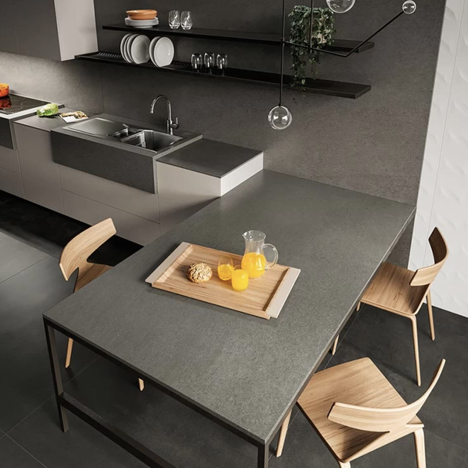 A modern kitchen featuring Basaltina Volcano grey countertops, complemented by wooden chairs, a metal table, open shelves, and a tray with a glass pitcher of orange juice, glasses, and pastries. The bright lighting enhances the minimalist design.