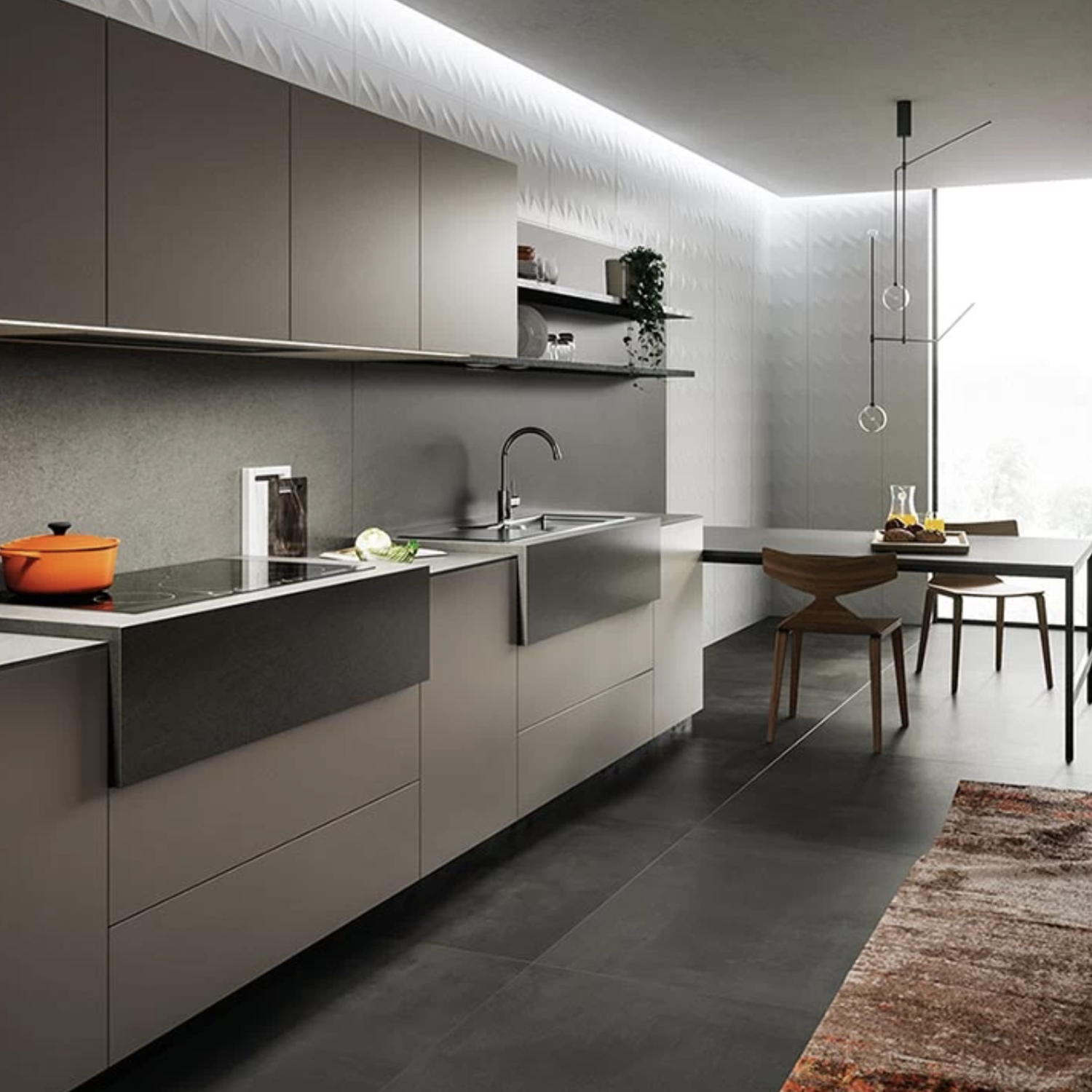 Modern kitchen featuring gray cabinets, a sleek sink, an orange pot on the stove, minimalist lighting, and a dining table with wooden chairs. The space is brightened by a textured Basaltina Volcano wall and a large window.