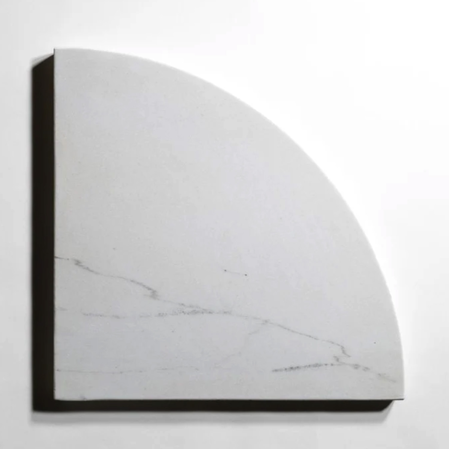 A quarter-circle slab of Colorado Calacatta marble from the Bath Accessories (Bevel Seat) collection, featuring faint gray veining, rests against a plain white background and casts a soft shadow to the right.