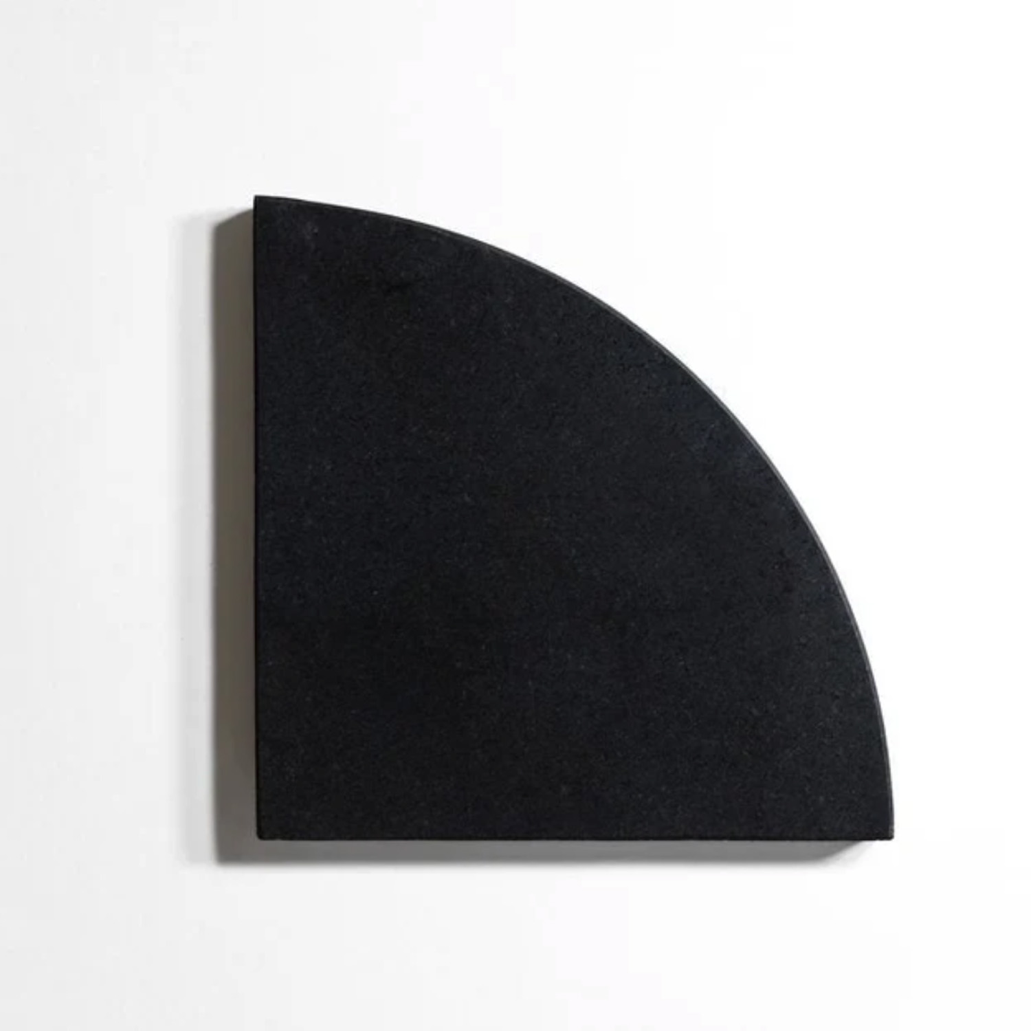 A black Bath Accessories (Corner Shelf) with a flat base and curved edge is displayed against a white background, creating a simple geometric contrast.
