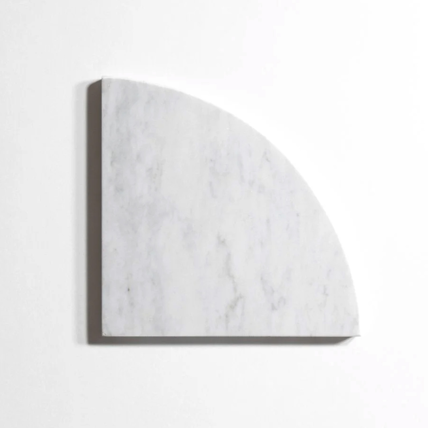 A Venatino Carrara Bath Accessories Corner Shelf, crafted from white marble with subtle gray veining, is mounted on a plain white wall, casting a faint shadow to the left and below.