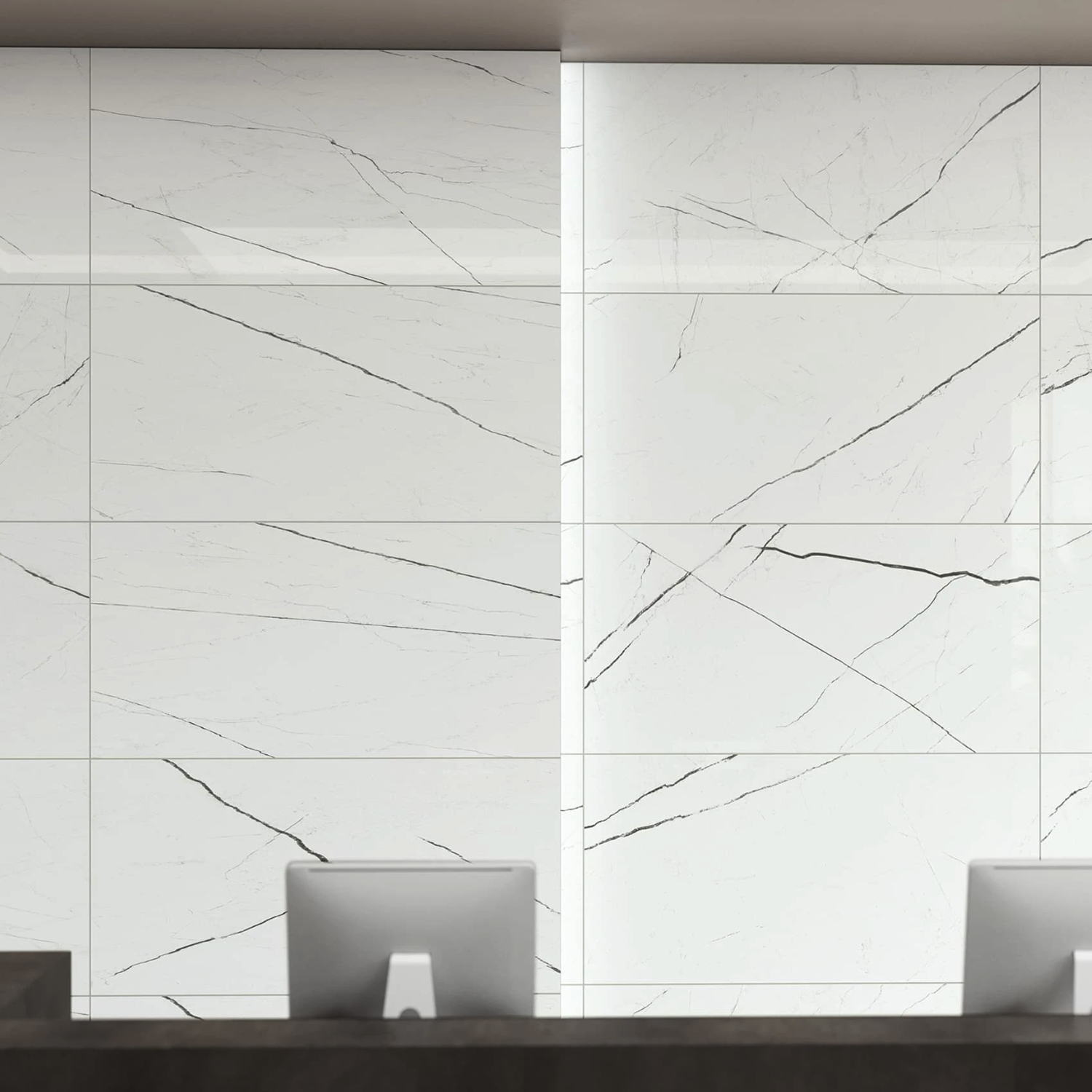 Two computer monitors sit on a dark counter in front of a wall clad with Beyond Calacatta - Glam White tiles, featuring prominent gray and black veining for a modern, minimalist look.