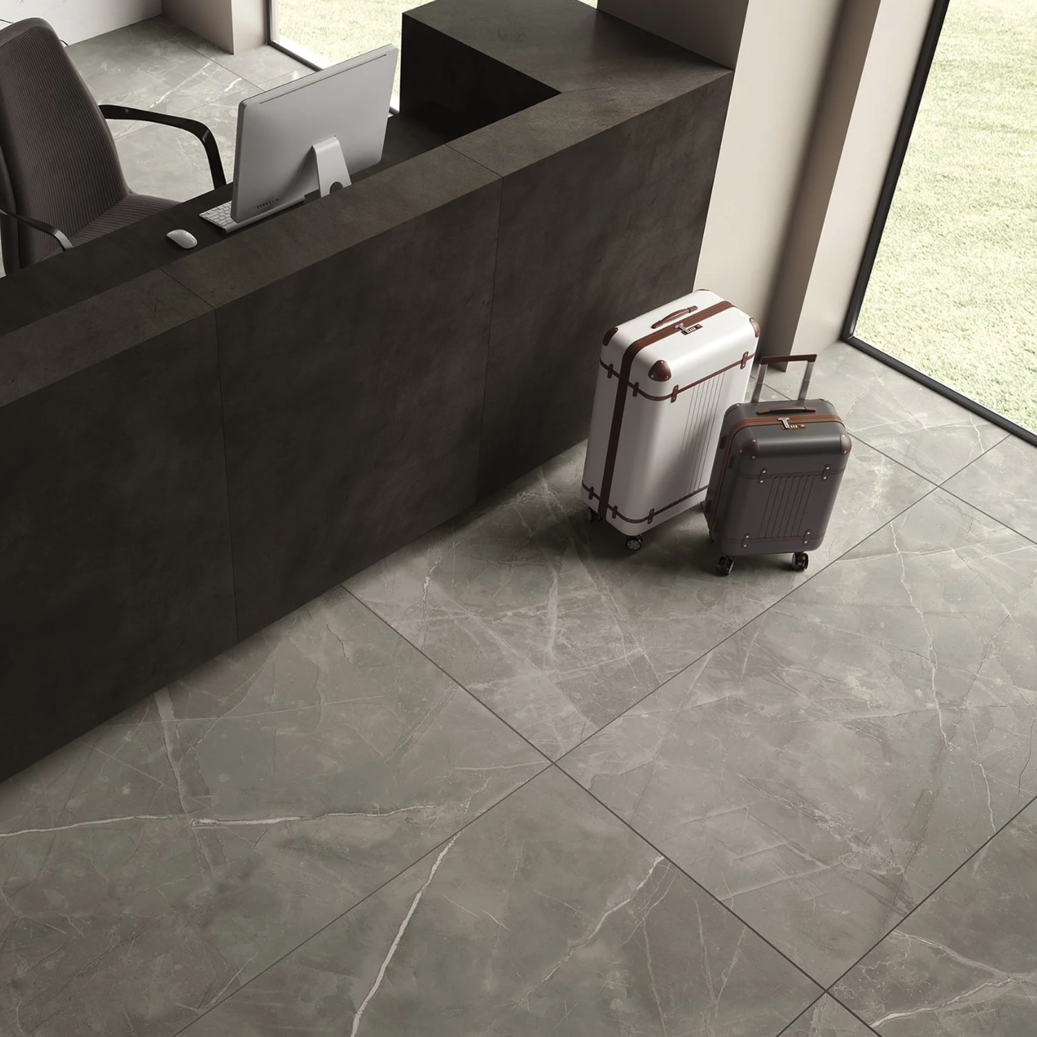 Two suitcases, one white and one brown, are placed near a modern dark reception desk. A computer monitor and office chair are behind the desk. The scene is completed by large Beyond Calacatta - Gray floor tiles and sunlight from the windows.