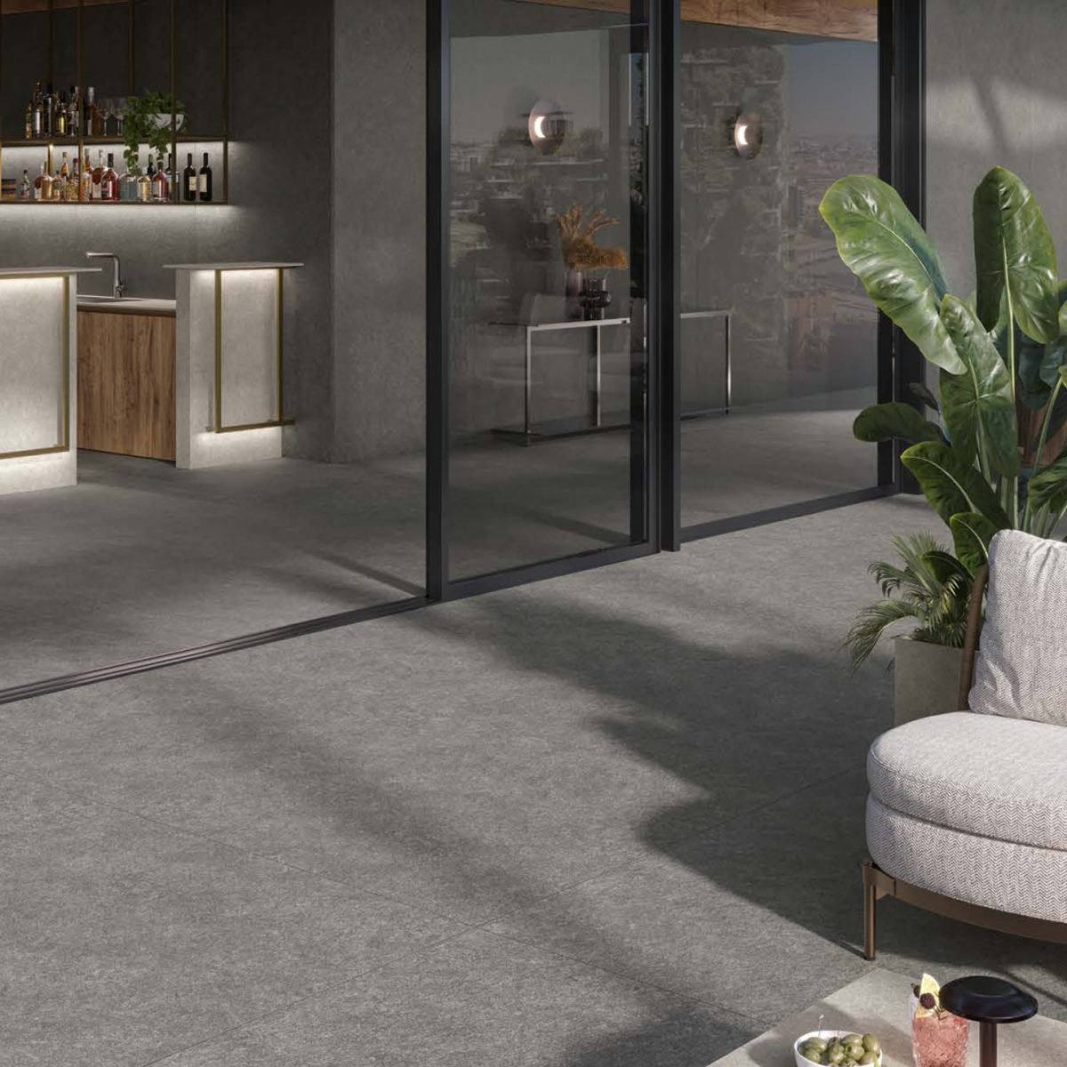 A modern indoor lounge features large glass walls, a bar with wooden accents, potted plants, and a gray cushioned chair in the foreground, all set atop a floor finished with Boost Mineral - Tarmac tiles.