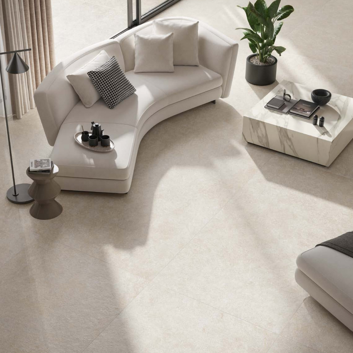 Here’s a rewritten version of your sentence using the given product data: A modern, sunlit living room featuring a curved white sofa with cushions, a small side table, a marble coffee table with decor, and a potted plant—all set atop Boost Mineral - White tiles.