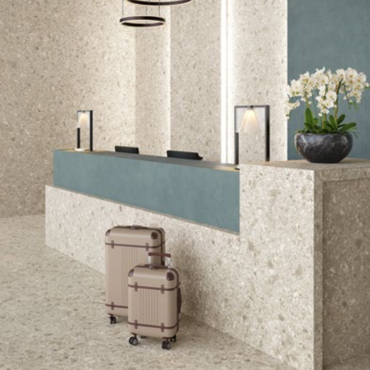 A hotel reception desk with two suitcases in front, modern lamps on the counter, and a large potted white orchid nearby, set against neutral Boost Mix - Ivory stone walls and flooring to create a clean, elegant atmosphere.