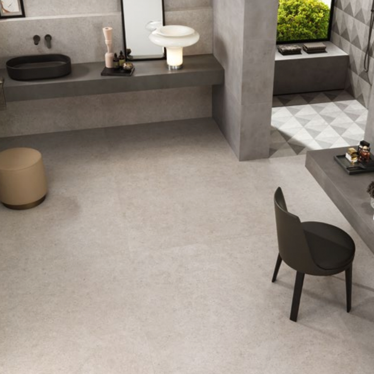 Modern bathroom featuring Boost Stone - Pearl on the walls and floors, a black sink, a round beige stool, a dark chair, and a large mirror. A small table with items sits nearby, with a green outdoor view visible through the window.
