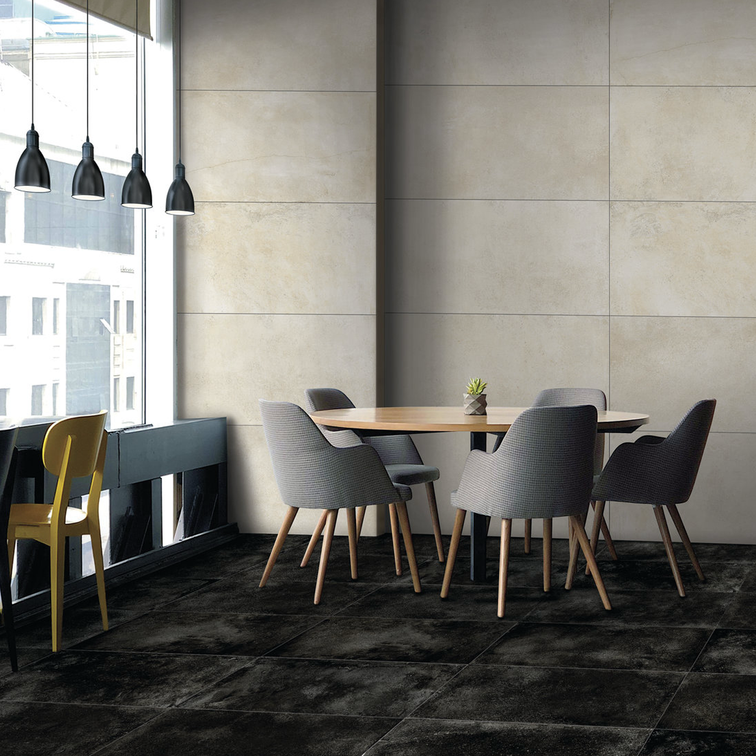 A modern dining area featuring a round wooden table, four gray chairs, and a small plant centerpiece, with a yellow chair placed at the Brooklyn - Cemento Black counter by large windows illuminated by hanging pendant lights.