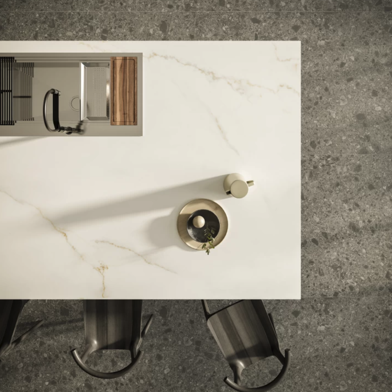 A top view of a Calacatta Apuano kitchen island with a sink, cutting board, vase, and bowl, next to three modern chairs on a gray speckled floor.