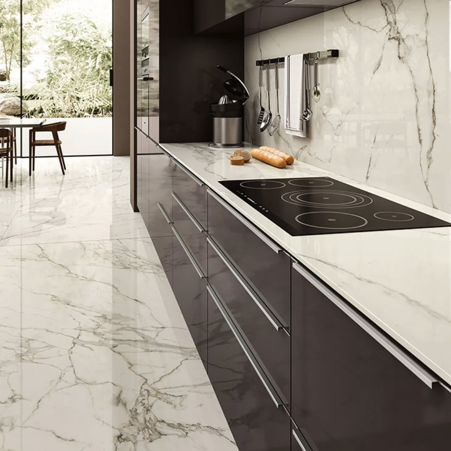 Modern kitchen featuring glossy cabinets and Calacatta Extra A marble floors and walls, an electric cooktop, and bread with a knife on the counter. Cooking utensils hang overhead, and a dining area with chairs is visible through a glass door.