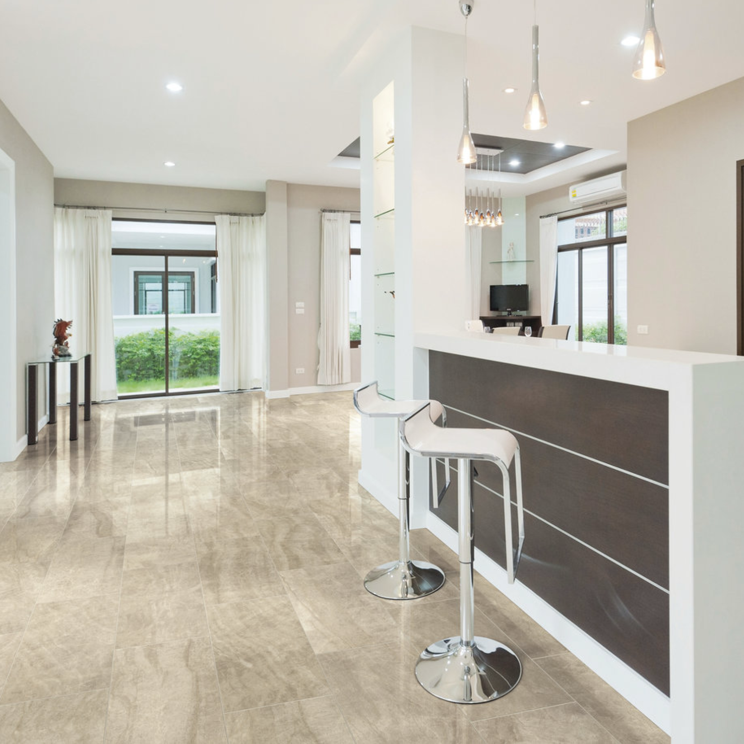 Contemporary, luminous living space featuring Carrara Select - Carrara Paonazzo glossy beige tile floors, a sleek white and dark wood bar area with two metal barstools, stylish pendant lights, expansive floor-to-ceiling windows, and sheer curtains that allow abundant natural light.
