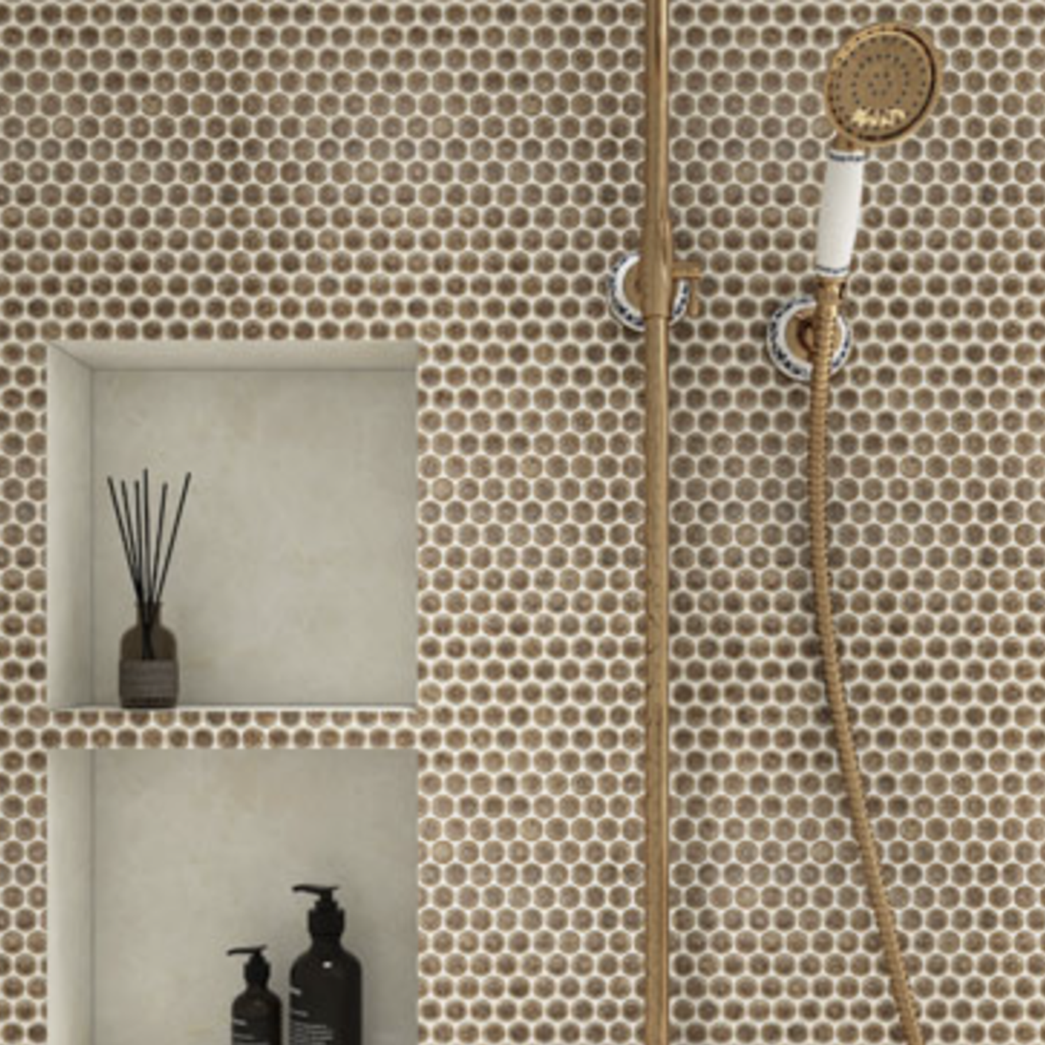 A shower wall featuring Chameleon - Rustic Sunset’s small round brown tiles, paired with a gold showerhead and two built-in shelves displaying black bottles and a reed diffuser.