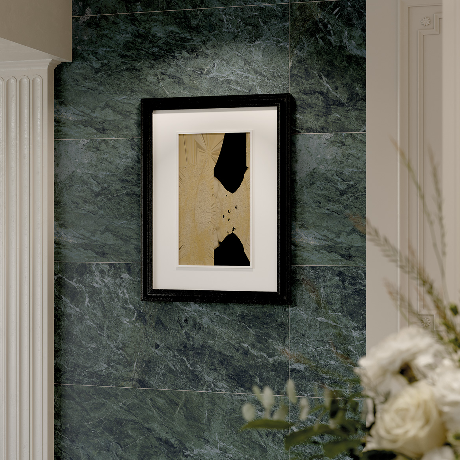 A black-framed abstract artwork hangs on a Classic Boutique - Apline Verde green marble wall near a white pillar, with part of a floral arrangement visible in the foreground.