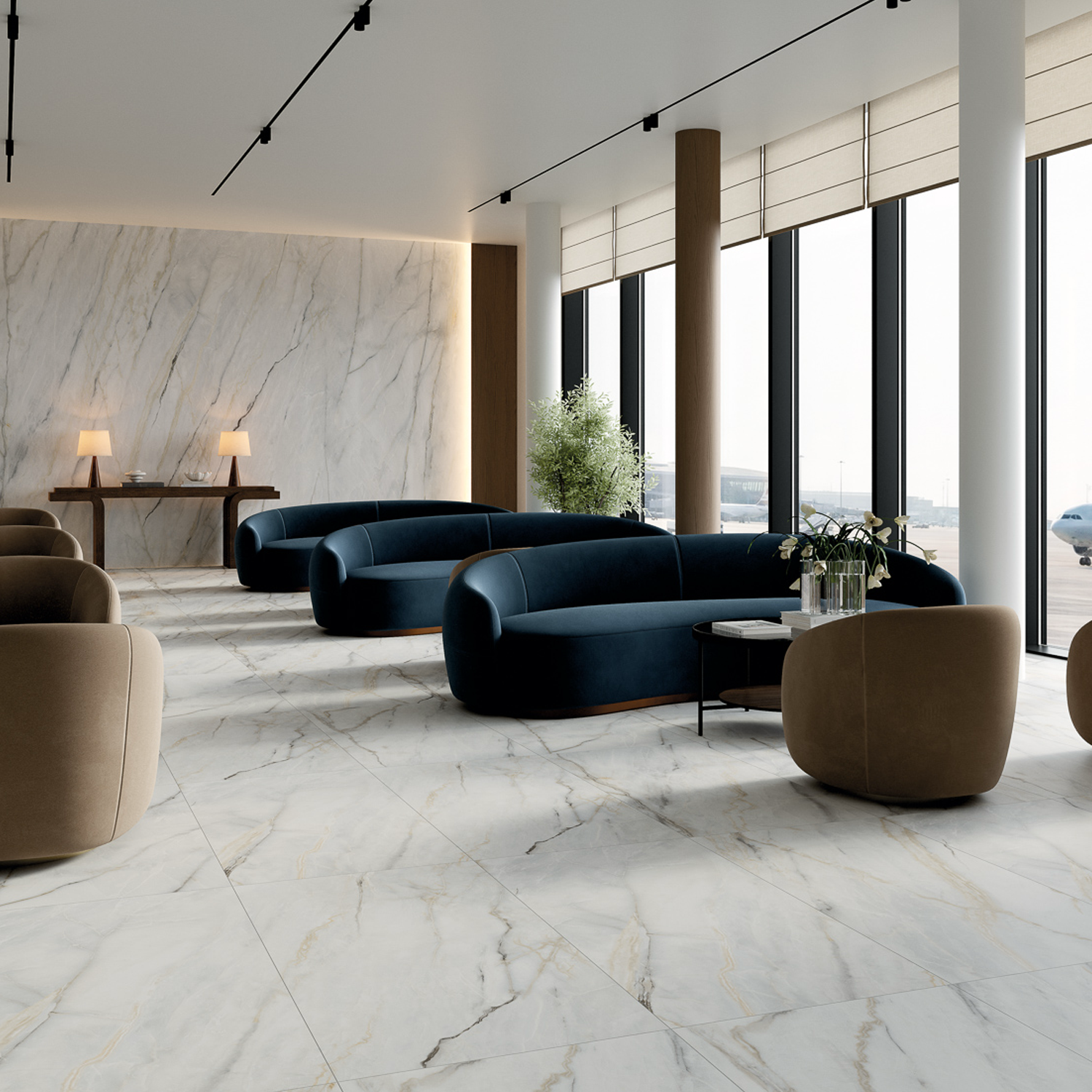 Modern lounge featuring Calacatta Bluette marble floors and walls, dark blue sofas, tan chairs, large windows welcoming natural light, and a console table with lamps. An airplane is visible outside.