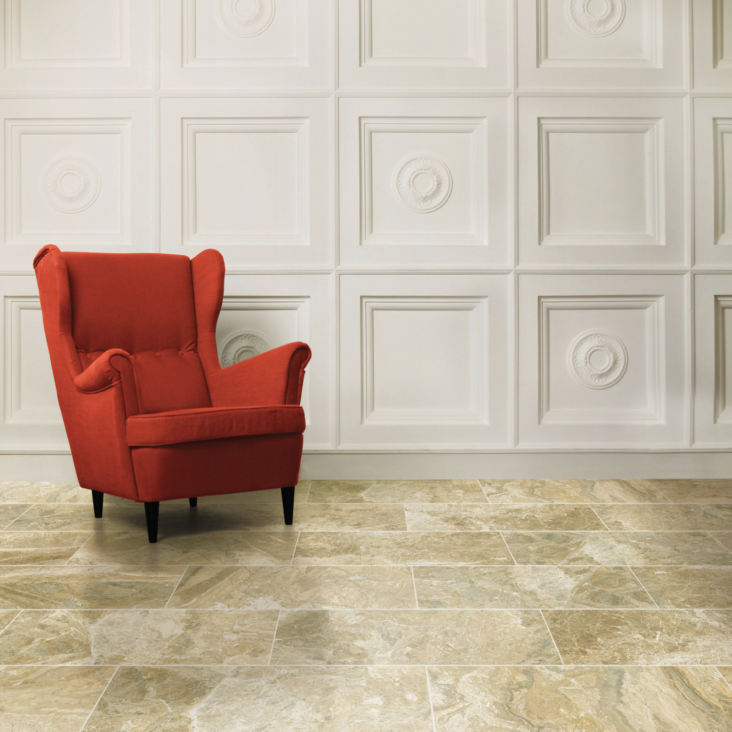 A red armchair sits on a Classic - Cremino beige marble tile floor in front of a white paneled wall with decorative square patterns.
