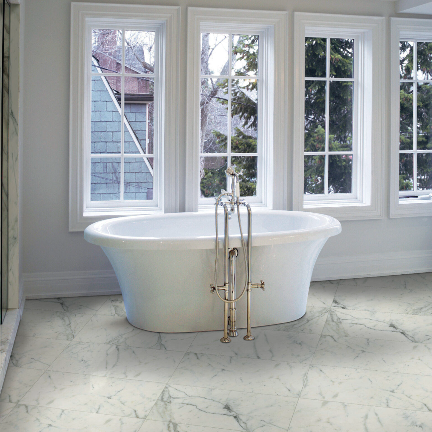 A Classic - Statuarietto freestanding bathtub with silver fixtures sits in front of three large windows overlooking trees. The bathroom features Classic - Statuarietto marble floors and walls, creating a bright, elegant atmosphere.