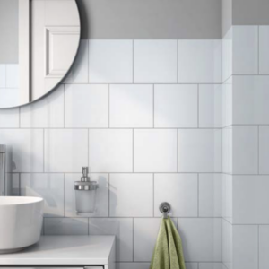 A bathroom featuring Color Collection - BG White Ice tiles on the walls, a round mirror, a white sink, a soap dispenser, and a light green towel hanging on a silver hook.