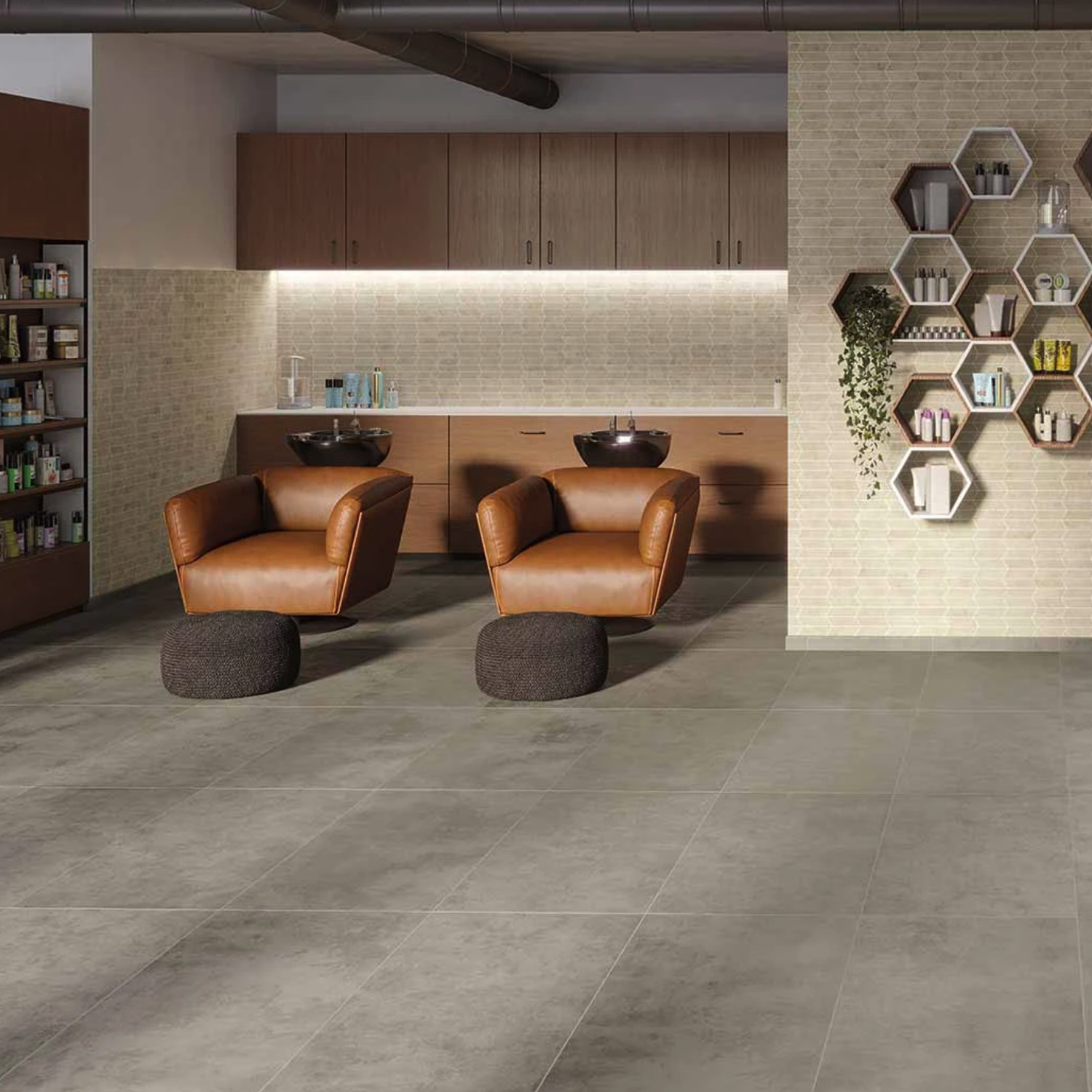 A modern salon features two brown leather chairs, round dark ottomans, wall-mounted sinks, wooden cabinets, a light brick backsplash, and hexagonal shelves displaying plants and products—all complemented by flooring in Cove - Fog.