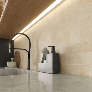 Modern kitchen counter with a black faucet, gray soap dispenser set, and bowl on a Cove Terra - Sand marble surface. Cream subway tiles and under-cabinet lighting create a warm, clean atmosphere.