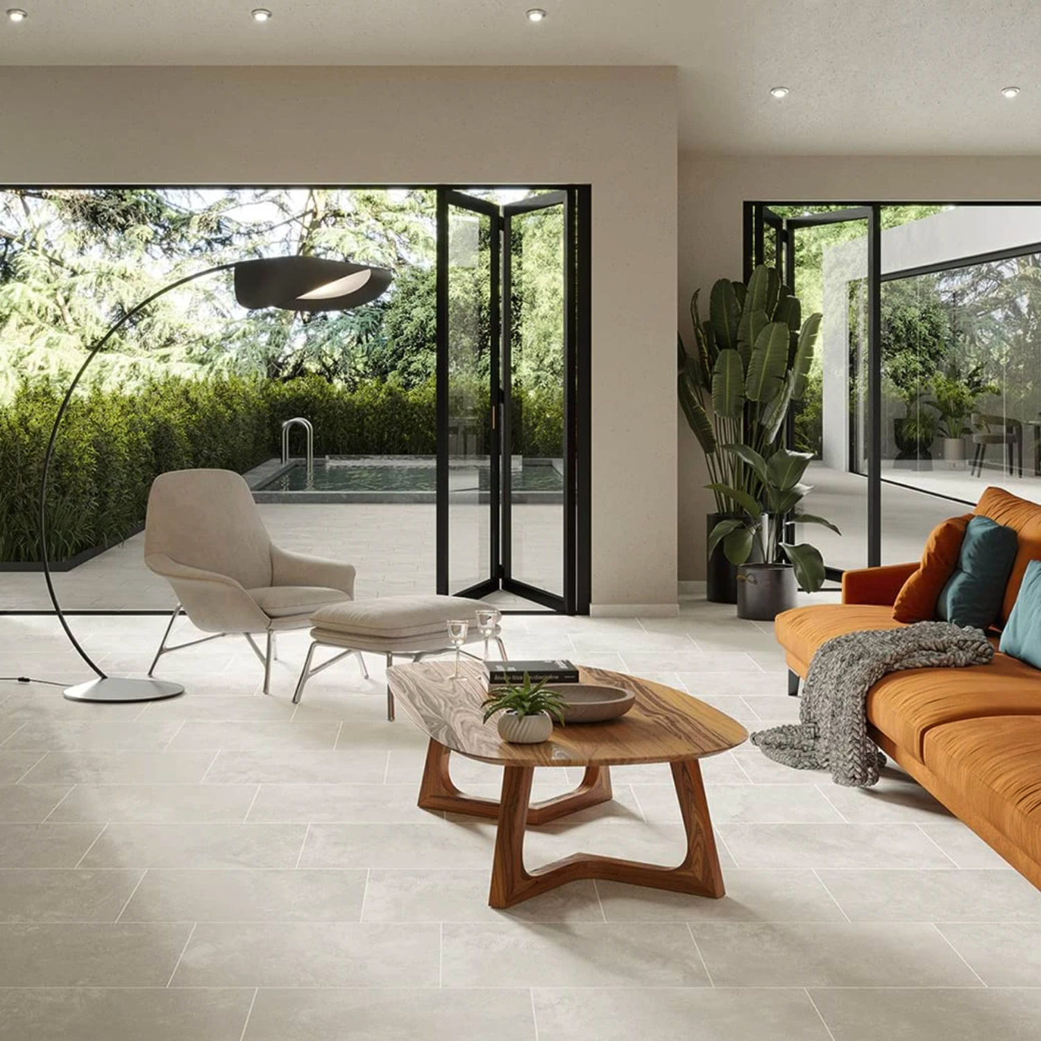 Modern living room featuring the Cove Terra - White chair, paired with an orange sofa, curved floor lamp, wooden coffee table, large potted plant, and sliding glass doors opening to a patio and pool surrounded by lush greenery.