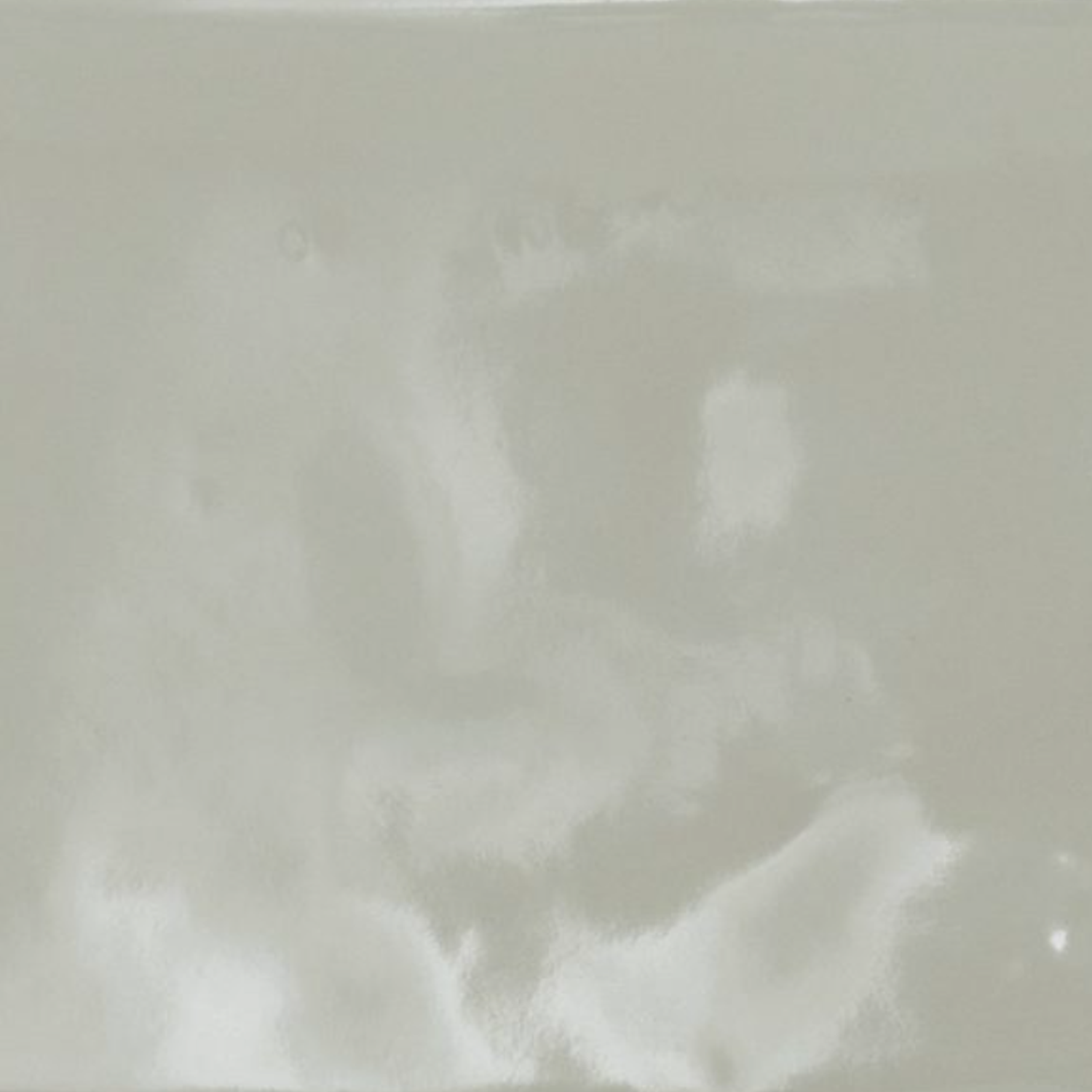 A close-up of the Cromia26 - Verde 2 glossy, light gray ceramic tile featuring subtle, cloudy white patterns and gentle reflections on its surface.