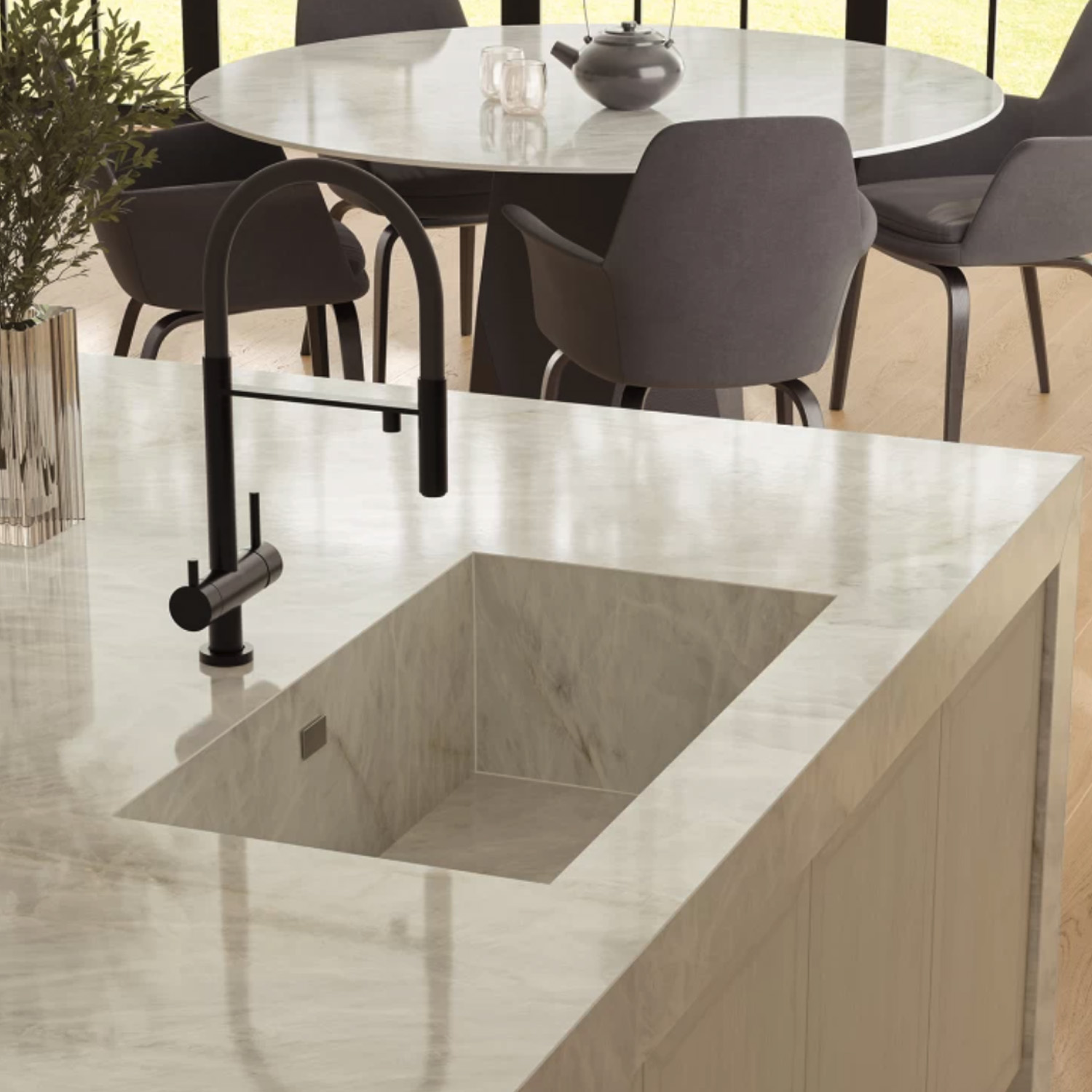 A modern kitchen featuring a Crystal White Bookmatch marble countertop with a built-in sink. In the background, a round dining table surrounded by four gray chairs is positioned near large windows that flood the space with natural light.