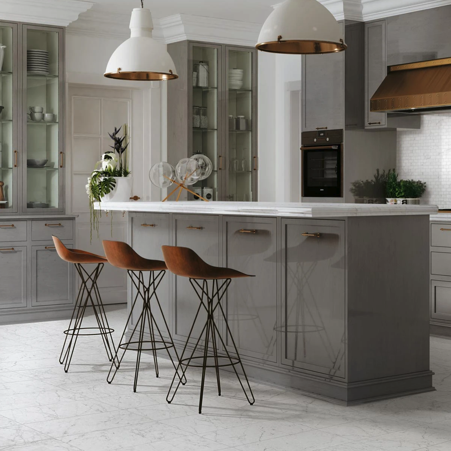 Modern kitchen featuring the Eon - Carrara island in gray, paired with three wooden bar stools, glass cabinets, pendant lights, and marble flooring. Greenery and decorative objects adorn the Eon - Carrara island, while stainless steel appliances can be seen in the background.