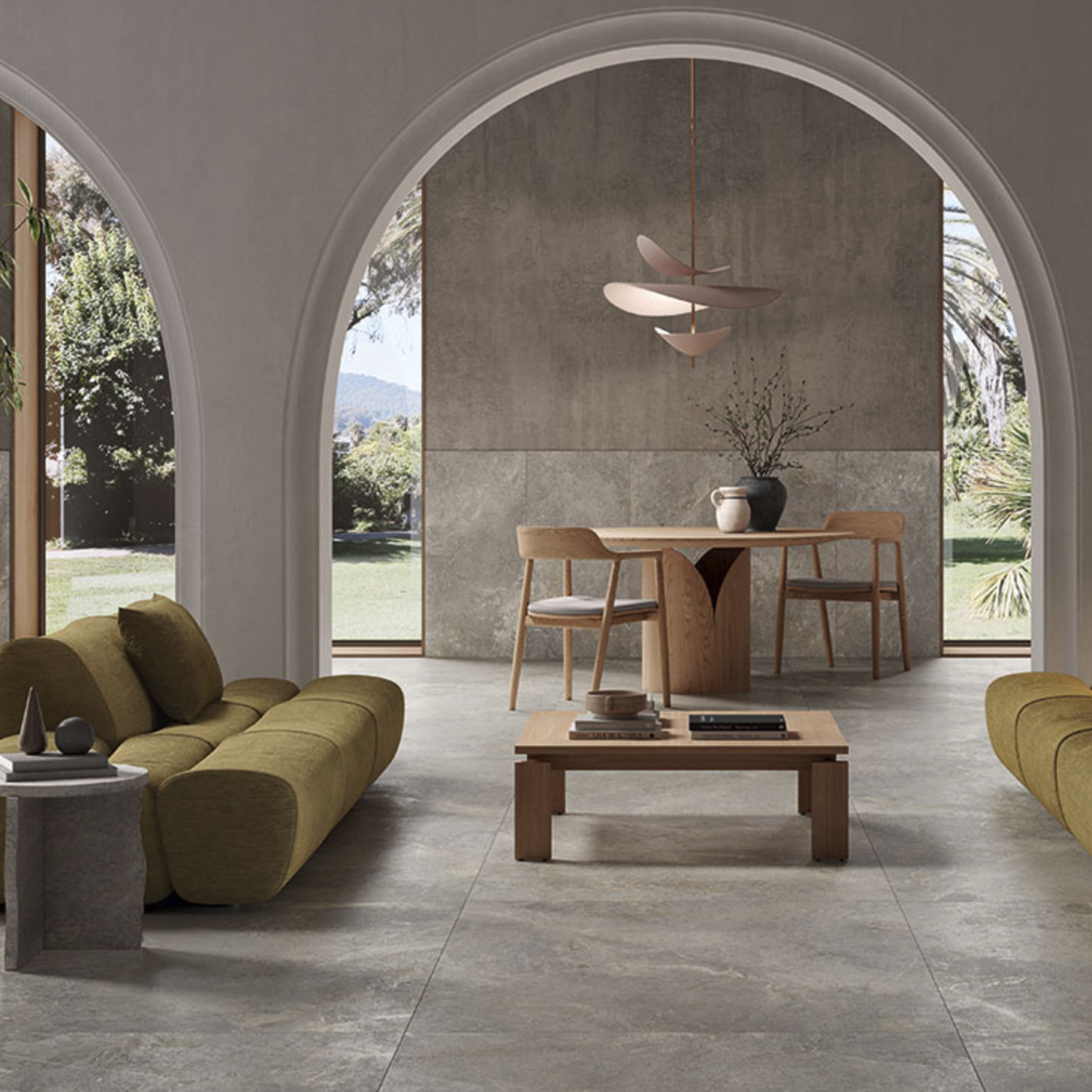 Modern living and dining area featuring Everstone - Ever Greige flooring, green sofas, a wooden coffee table, arched doorways, large windows overlooking the garden, and a minimalist dining table with chairs beneath a decorative pendant light.