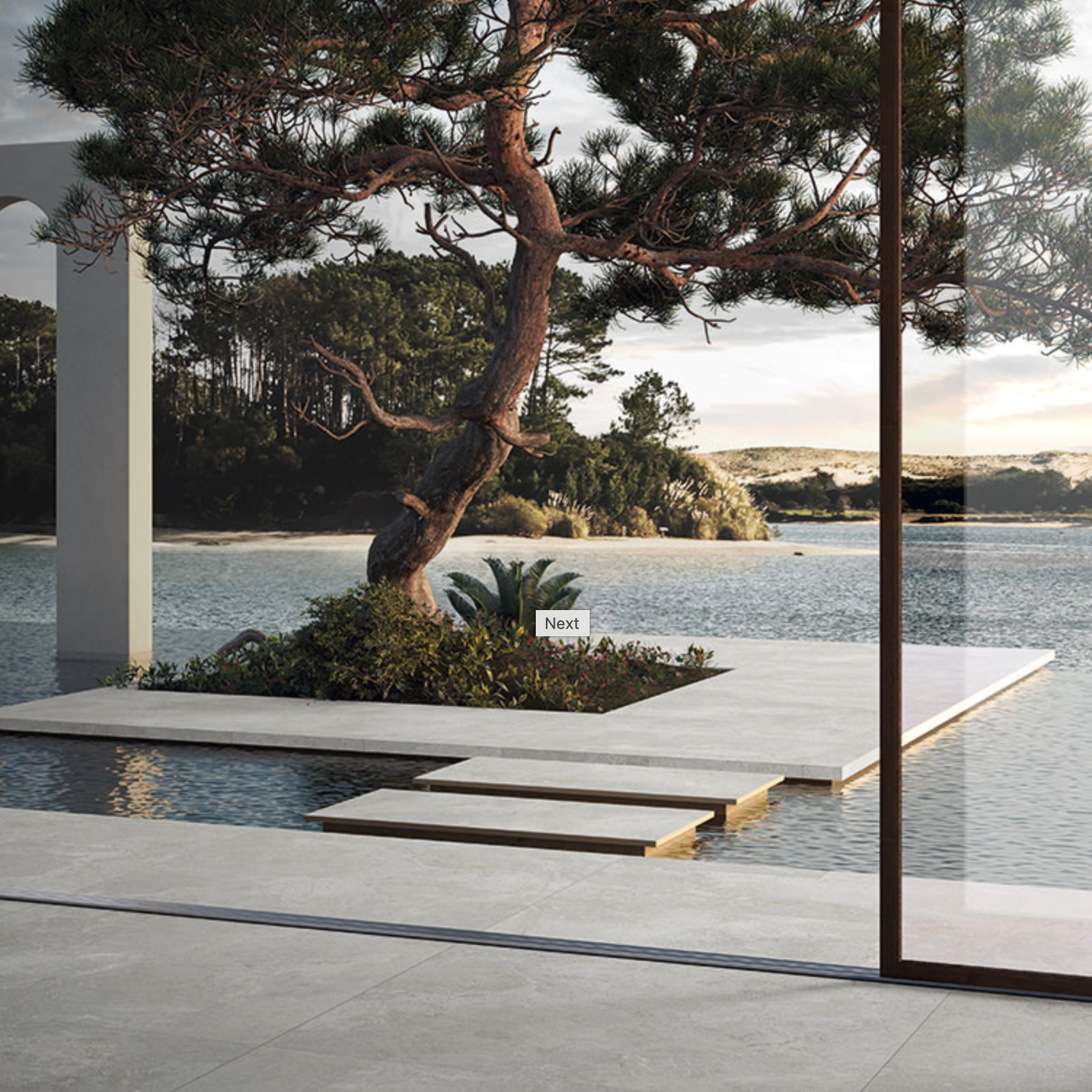 A modern outdoor space features a tree growing from a small island surrounded by water, with stone steps of Everstone - Ever White leading across, set against a backdrop of a forested shoreline.