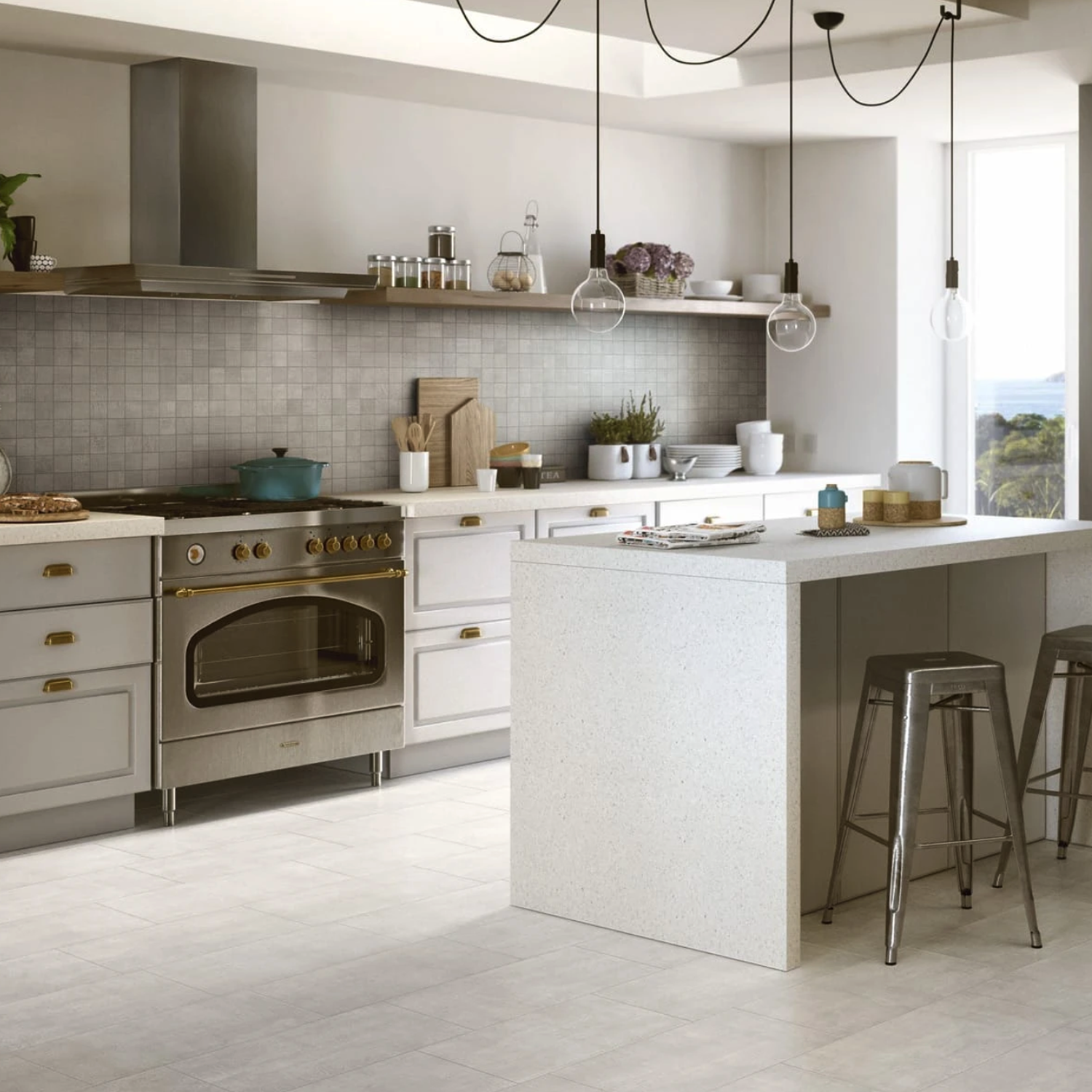 A modern kitchen featuring Fray - White cabinets, a stainless steel oven, a white island paired with metal stools, stylish pendant lights suspended above, and a tiled backsplash. The shelf is adorned with decorative items, while the window frames a scenic outdoor view.