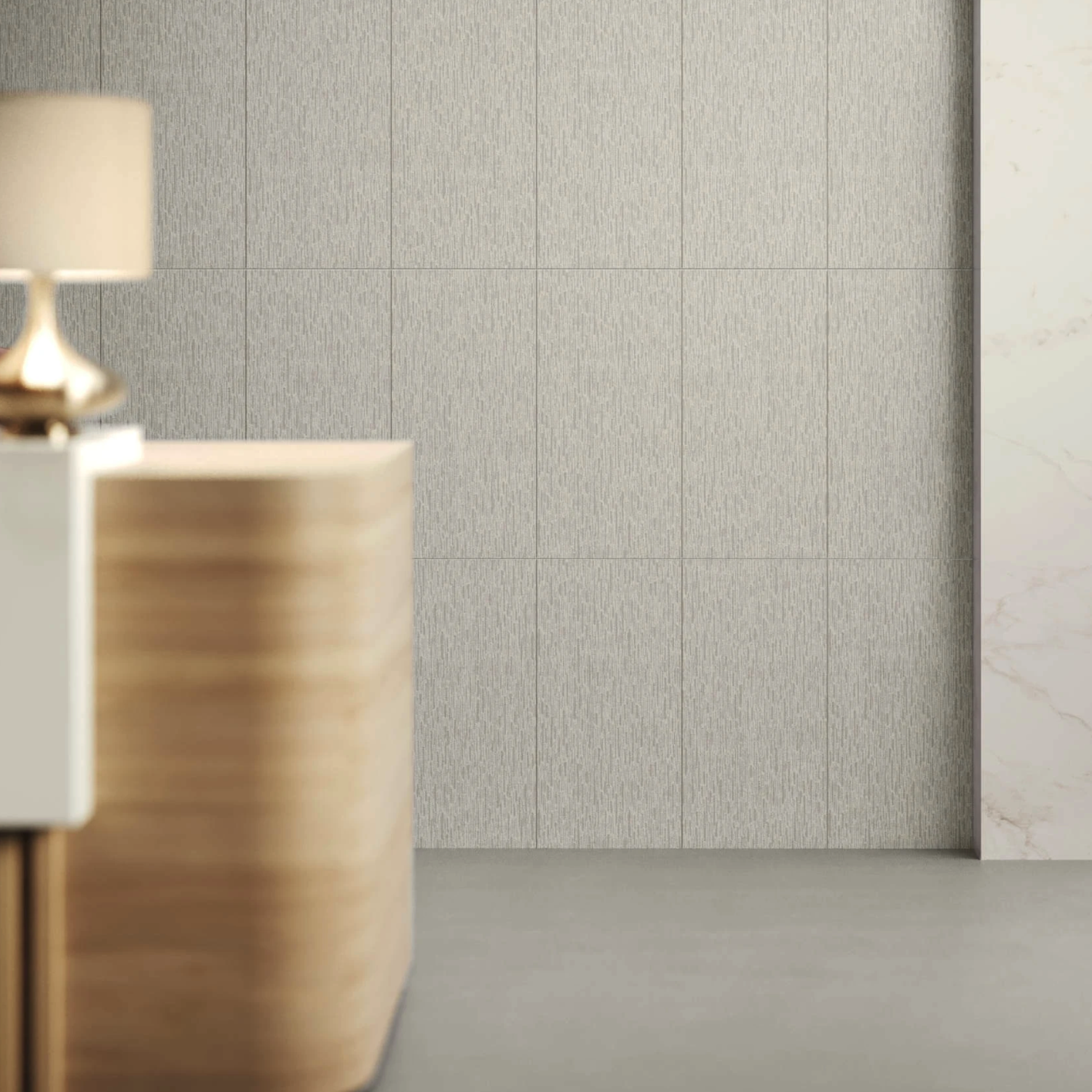A minimalist interior featuring a wooden front desk, a lamp, and a sleek gray tiled wall clad in Fray X - Trama Mist, with a partial glimpse of a marble accent wall on the right. The space exudes modernity and cleanliness.