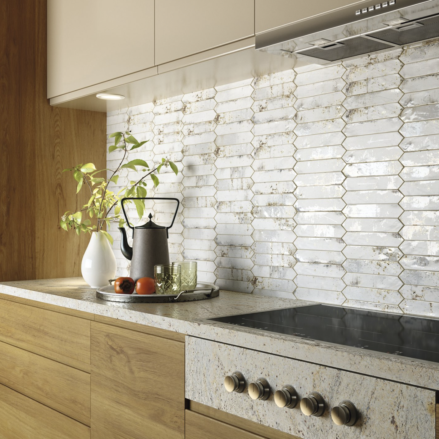 Modern kitchen featuring light wood cabinets, a speckled countertop, a teapot, glassware, vase with plant, tomatoes, and a backsplash in Grunge - Iron tiles in shades of white and gray. An electric stovetop is visible in the foreground.