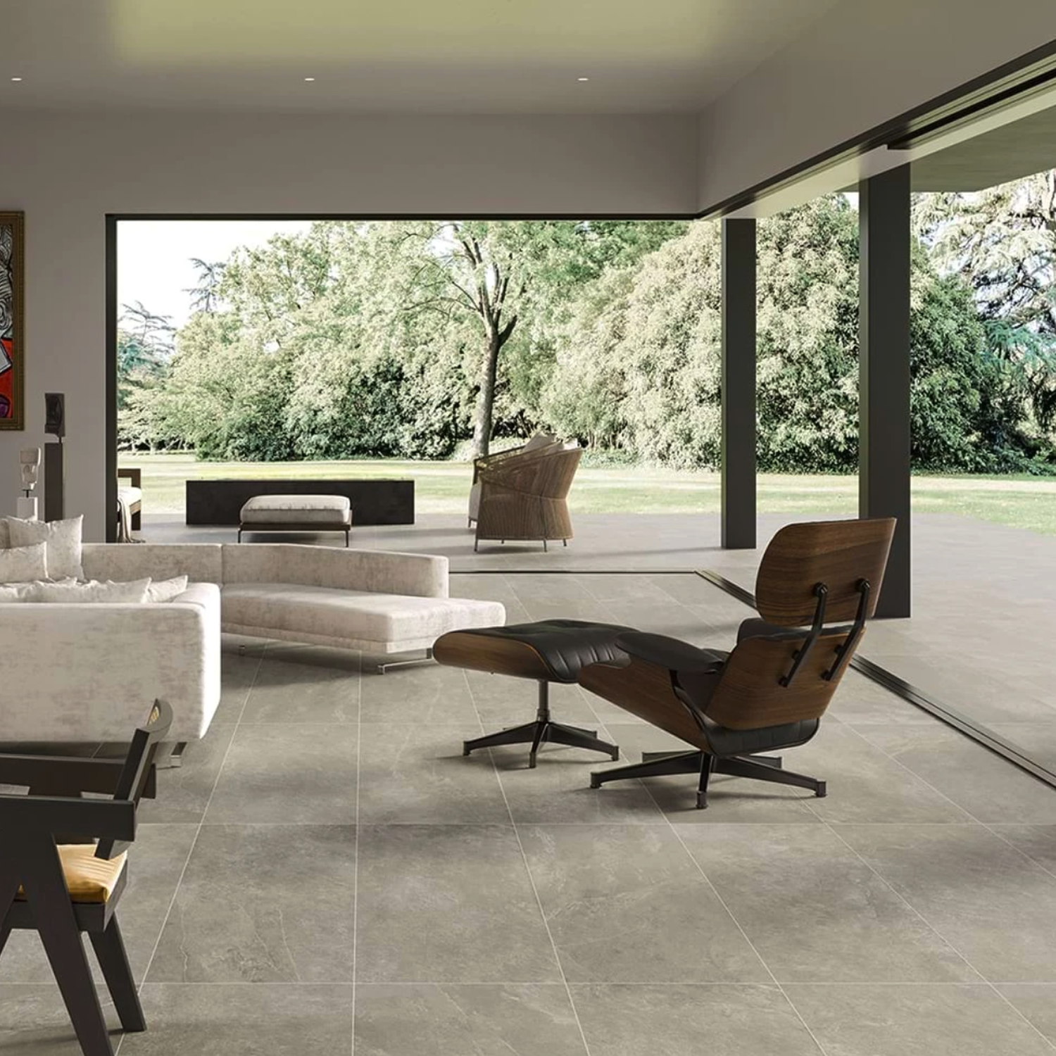 Modern living room featuring the Hero - Silver lounge chair and sofa, with large sliding glass doors opening to a patio and lush green trees outside, flooding the space with natural light.