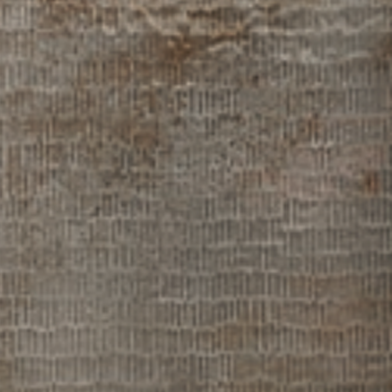 A close-up of the Inciso - Pebble surface, showcasing its textured, weathered appearance with a grid-like pattern and brownish stains that evoke the look of aged fabric or parchment.