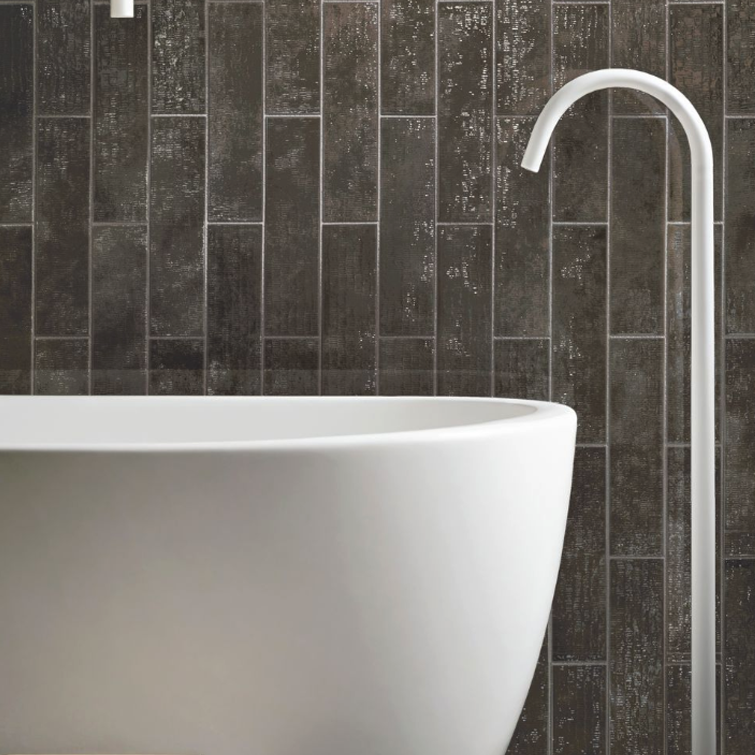 Close-up of the Inciso - Porphyr modern white bathtub with a curved silver faucet, set against a dark, vertically patterned textured tile wall.