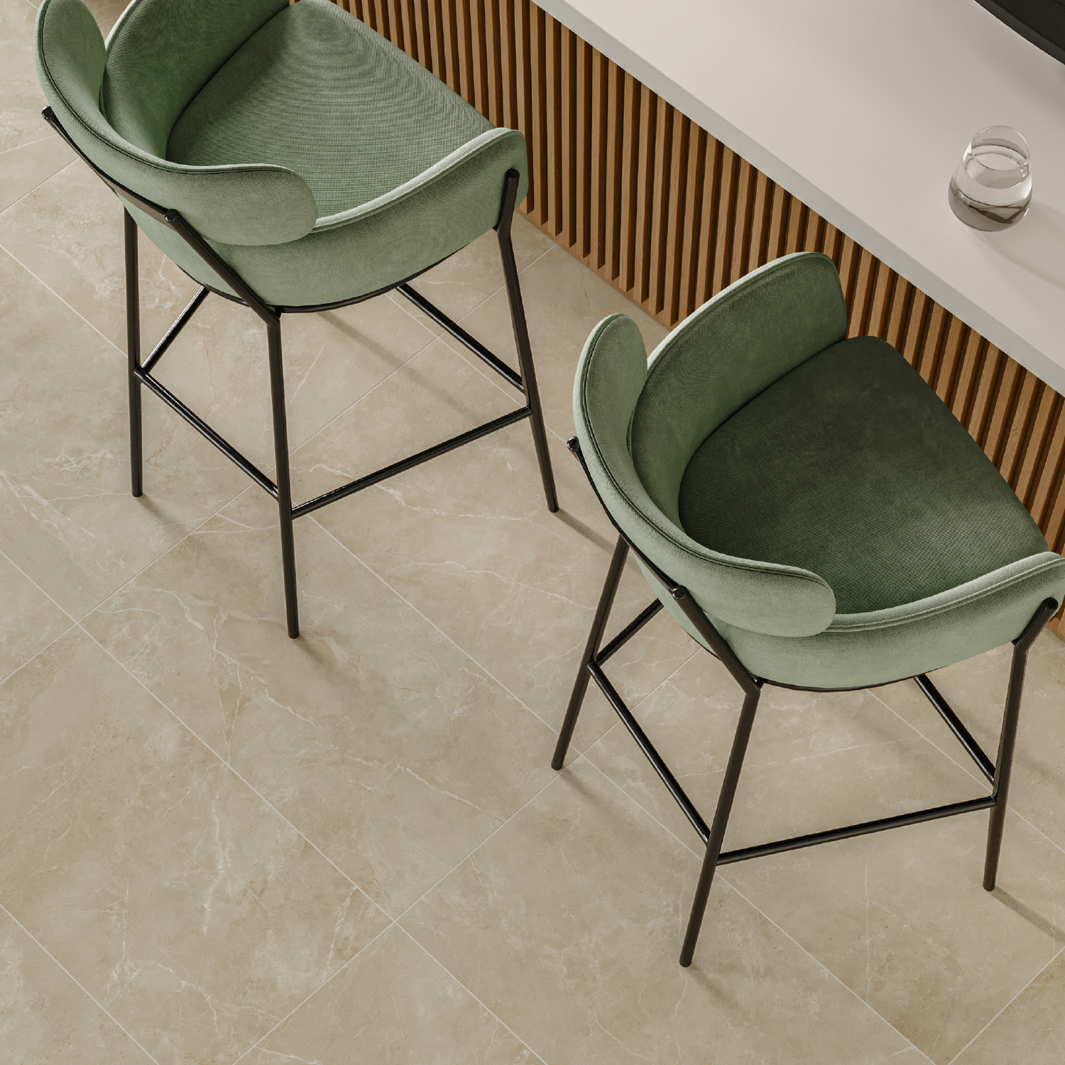 Two green barstools with black legs are positioned next to a light-colored countertop and a wooden, slatted panel. The floor features Keystone 2.0 - Bone tiles, and a glass sits on the counter.